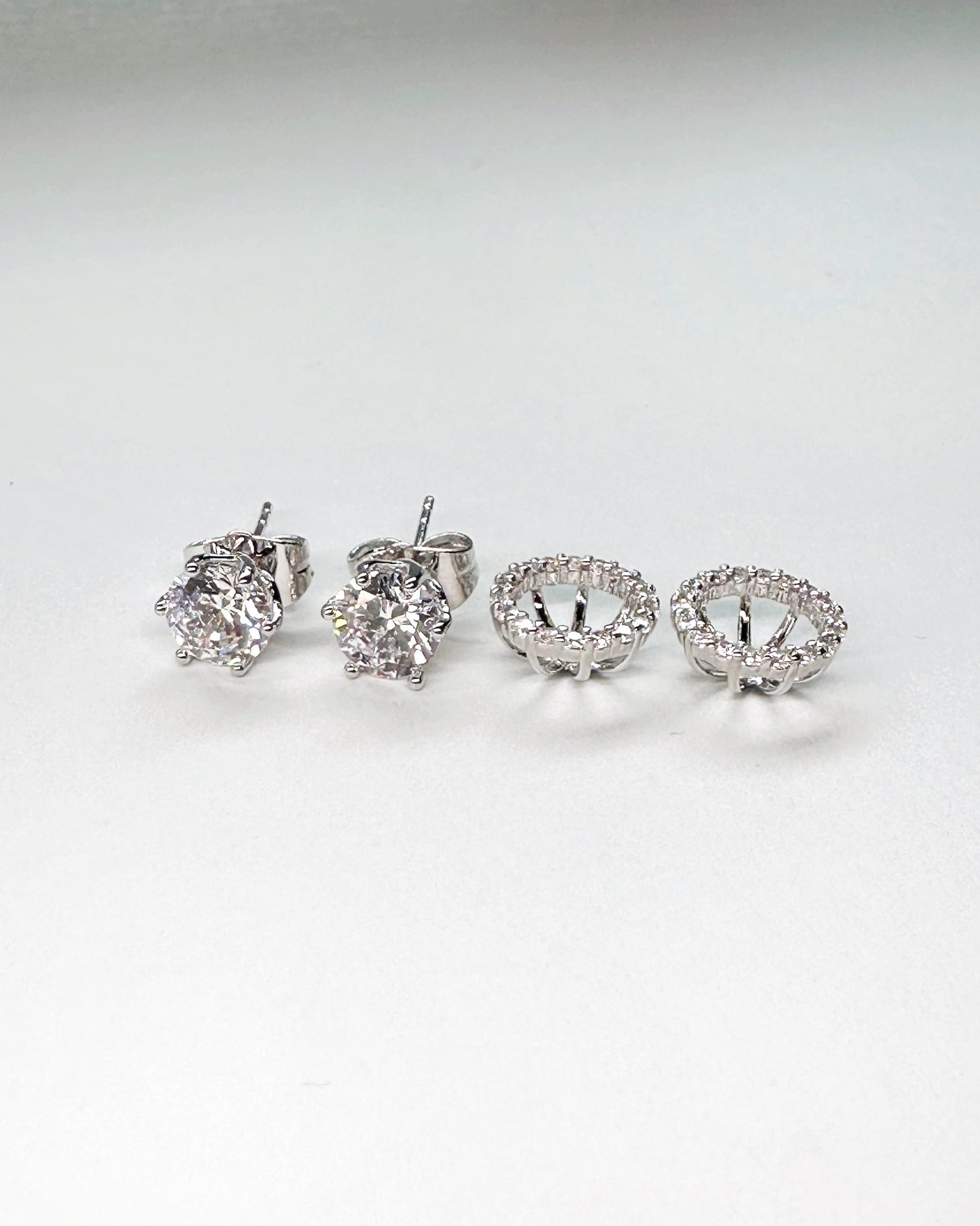 Side-by-side display of cubic zirconia halo stud earrings with round-cut center stones and open gallery setting in silver finish