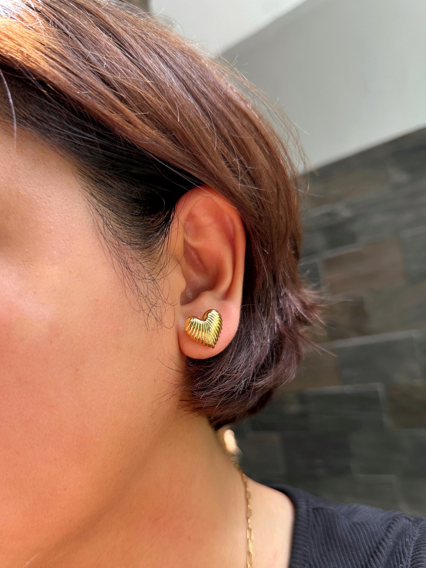 Model’s profile wearing stainless steel gold-tone ribbed heart earring in natural light