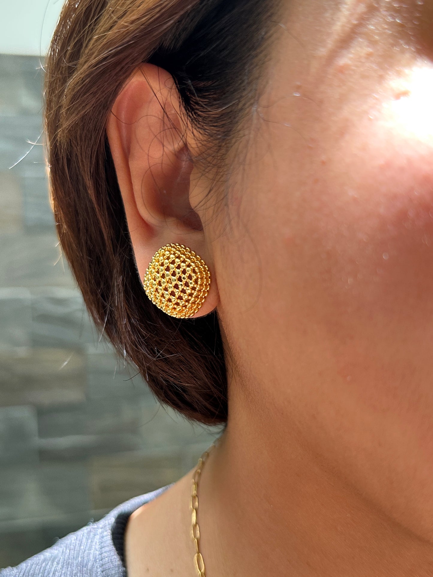 Close-up of textured gold button stud earring worn on ear in natural lighting