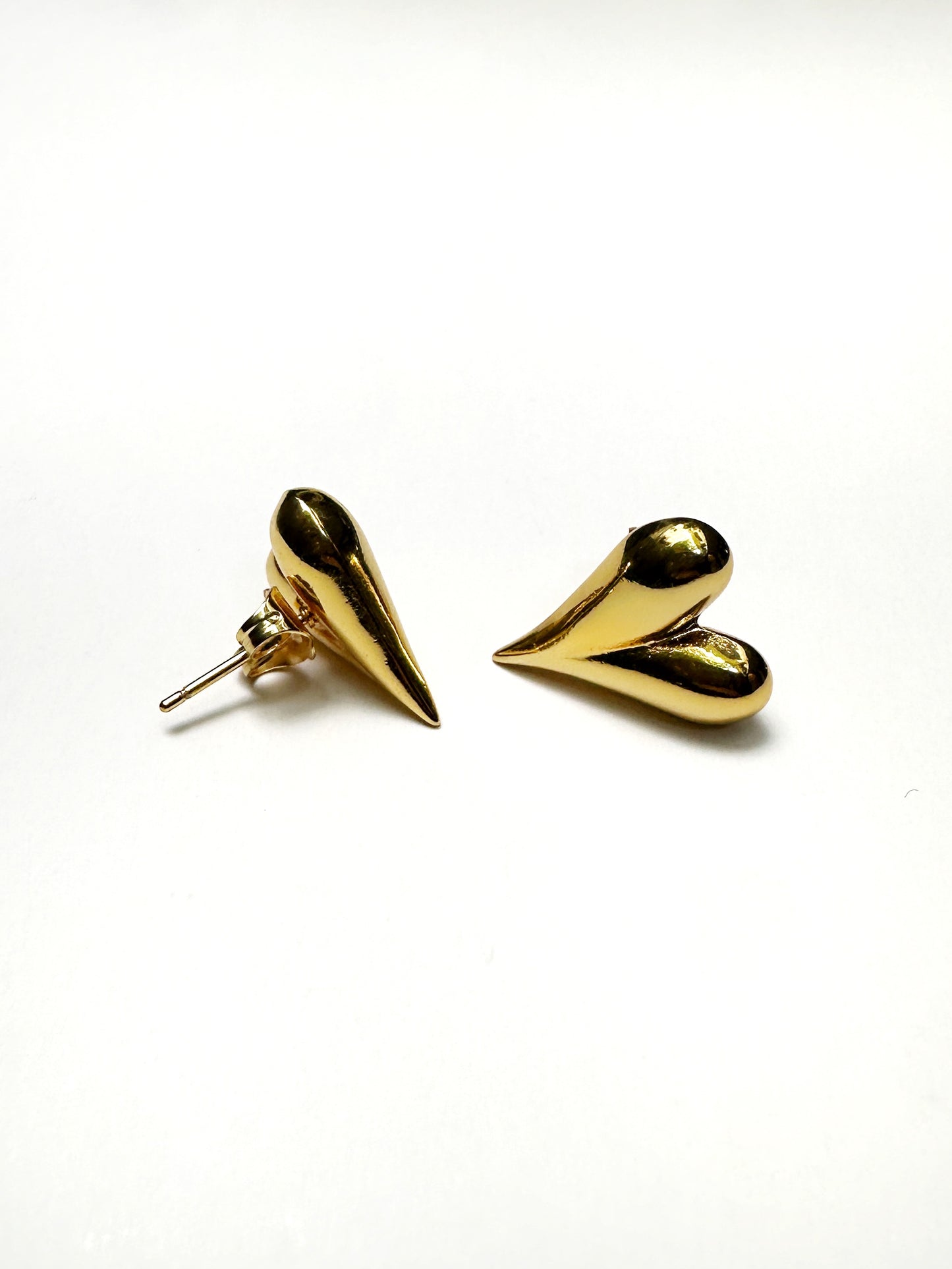 Angled view of gold puff heart earrings highlighting curved design