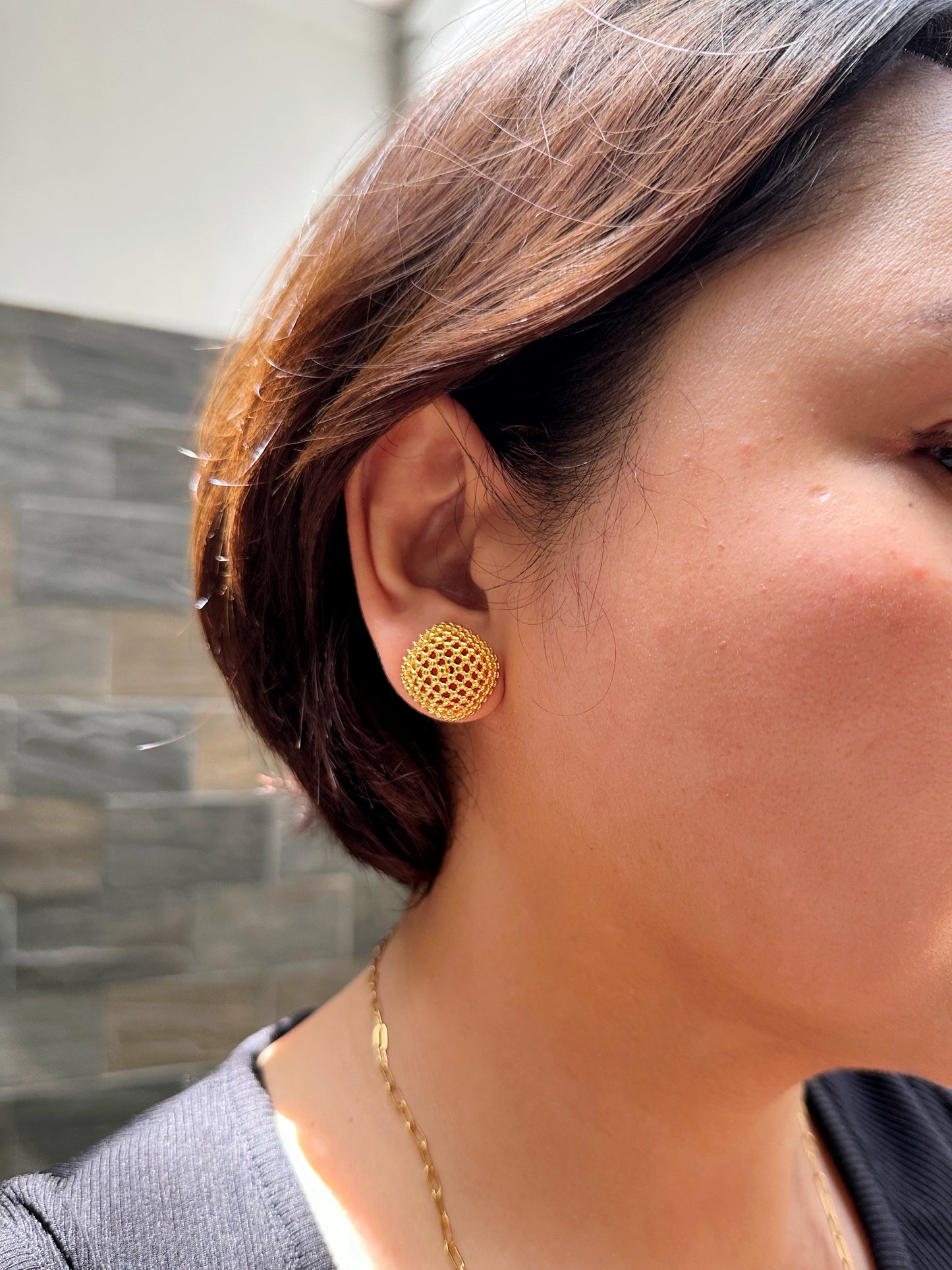 Side angle of woman wearing bold gold-tone mesh earrings