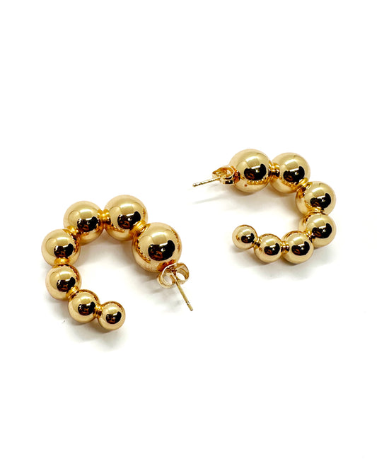 Chunky statement gold beaded hoop earrings laid flat on white background