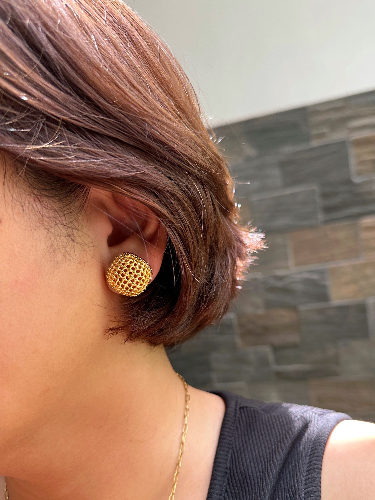 Model wearing large gold-tone mesh button stud earrings with short hair