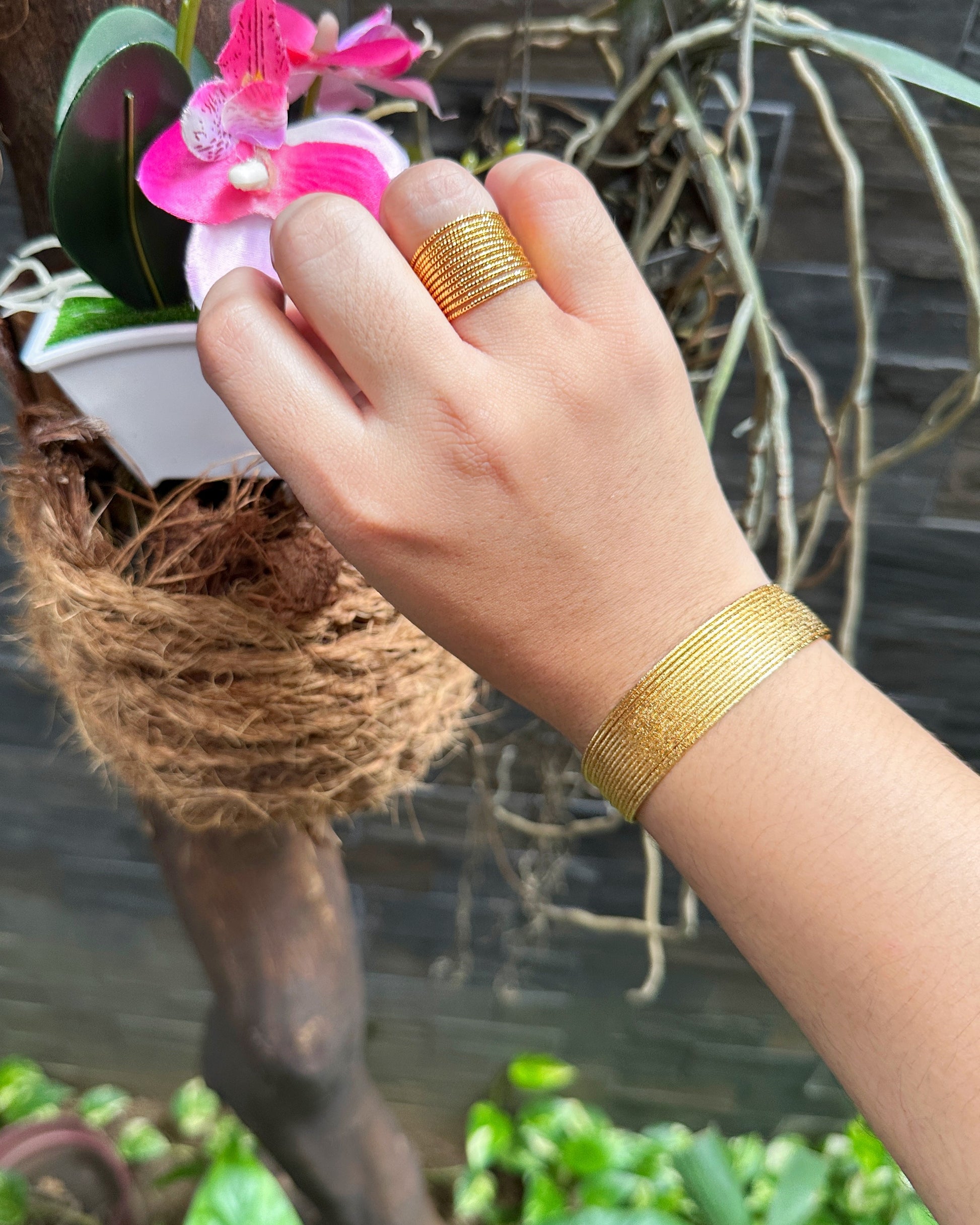 Gold cuff and ring worn on hand in garden setting with orchid