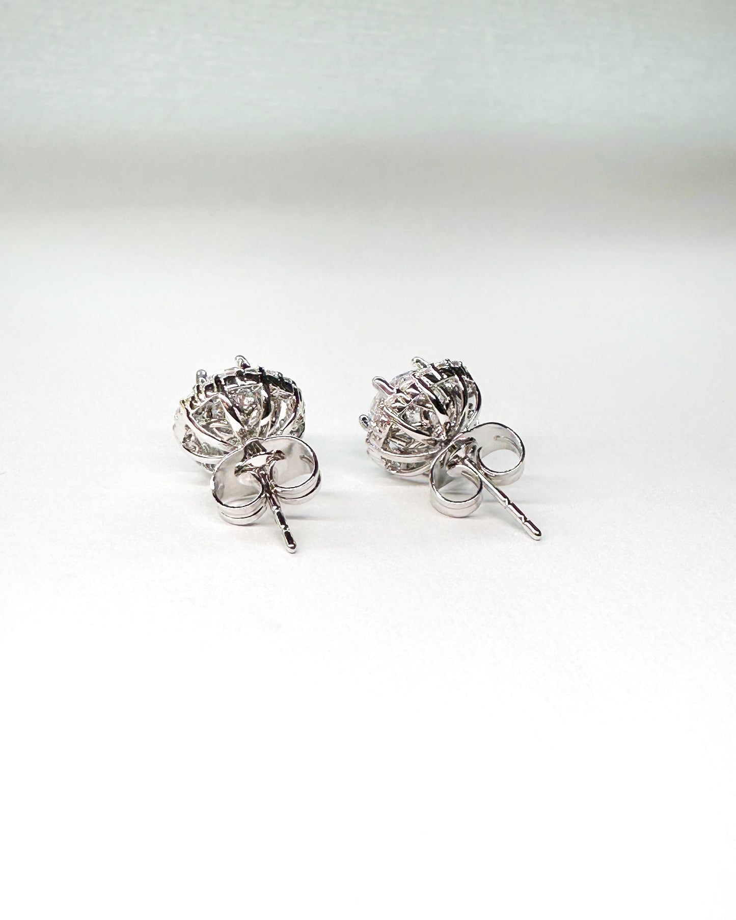 Back view of round-cut halo stud earrings with silver butterfly push backs, showcasing the open gallery basket setting and premium-grade cubic zirconia stones on a white background