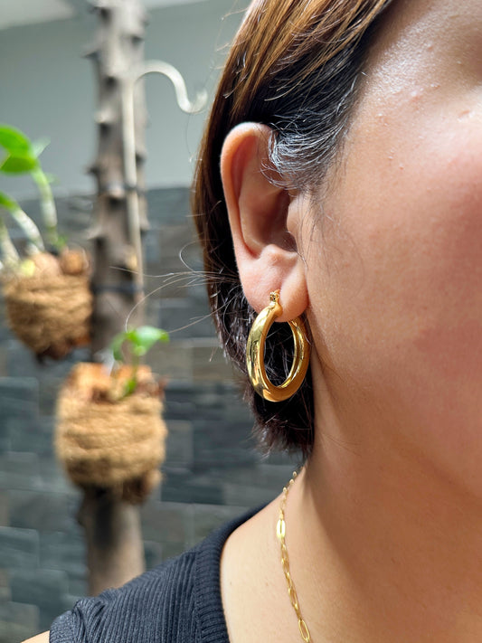 Woman wearing gold chunky hoop earrings, showing fit and shine on ear
