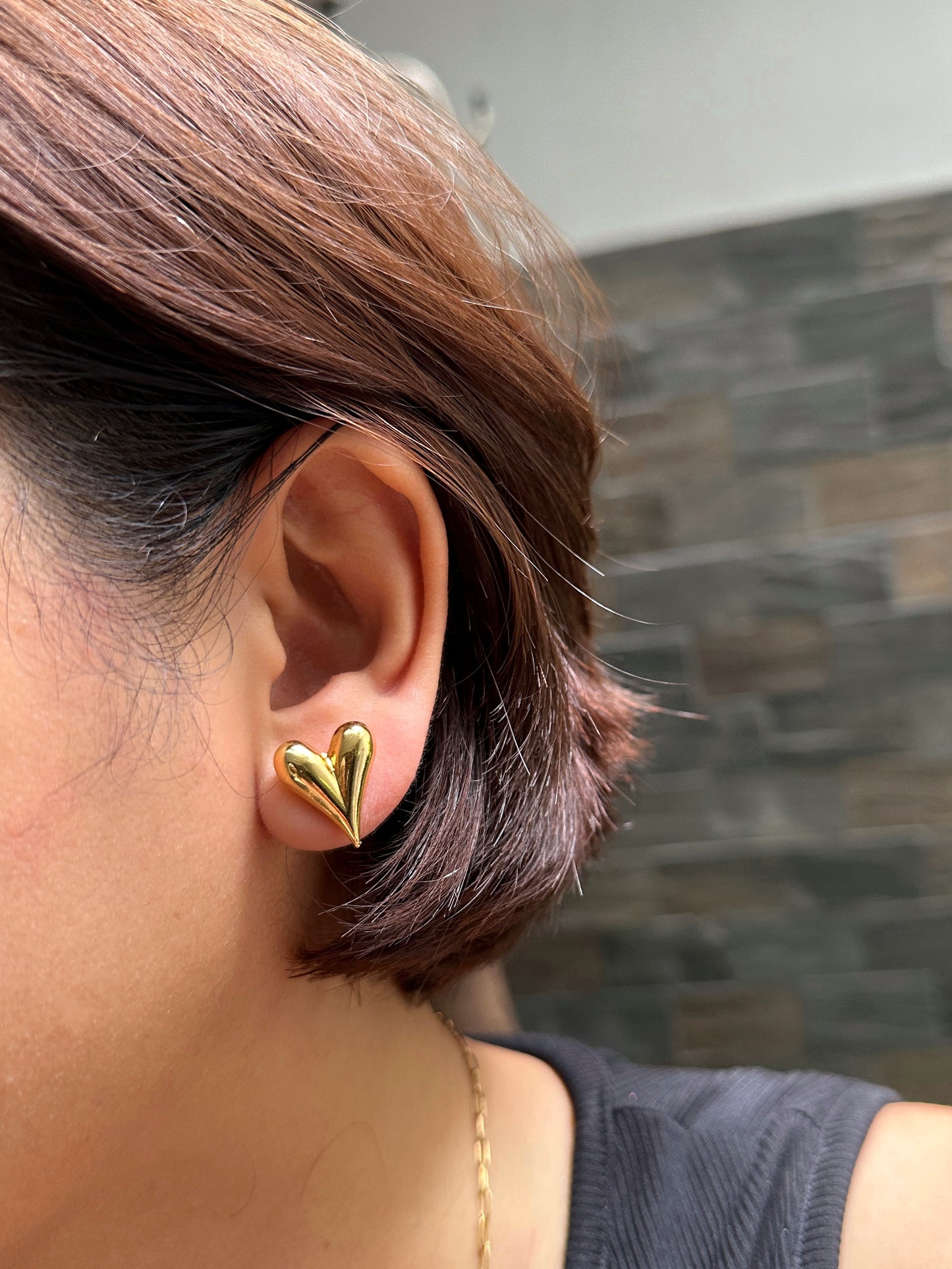 Model wearing gold puff heart stud earrings on ear with short hair