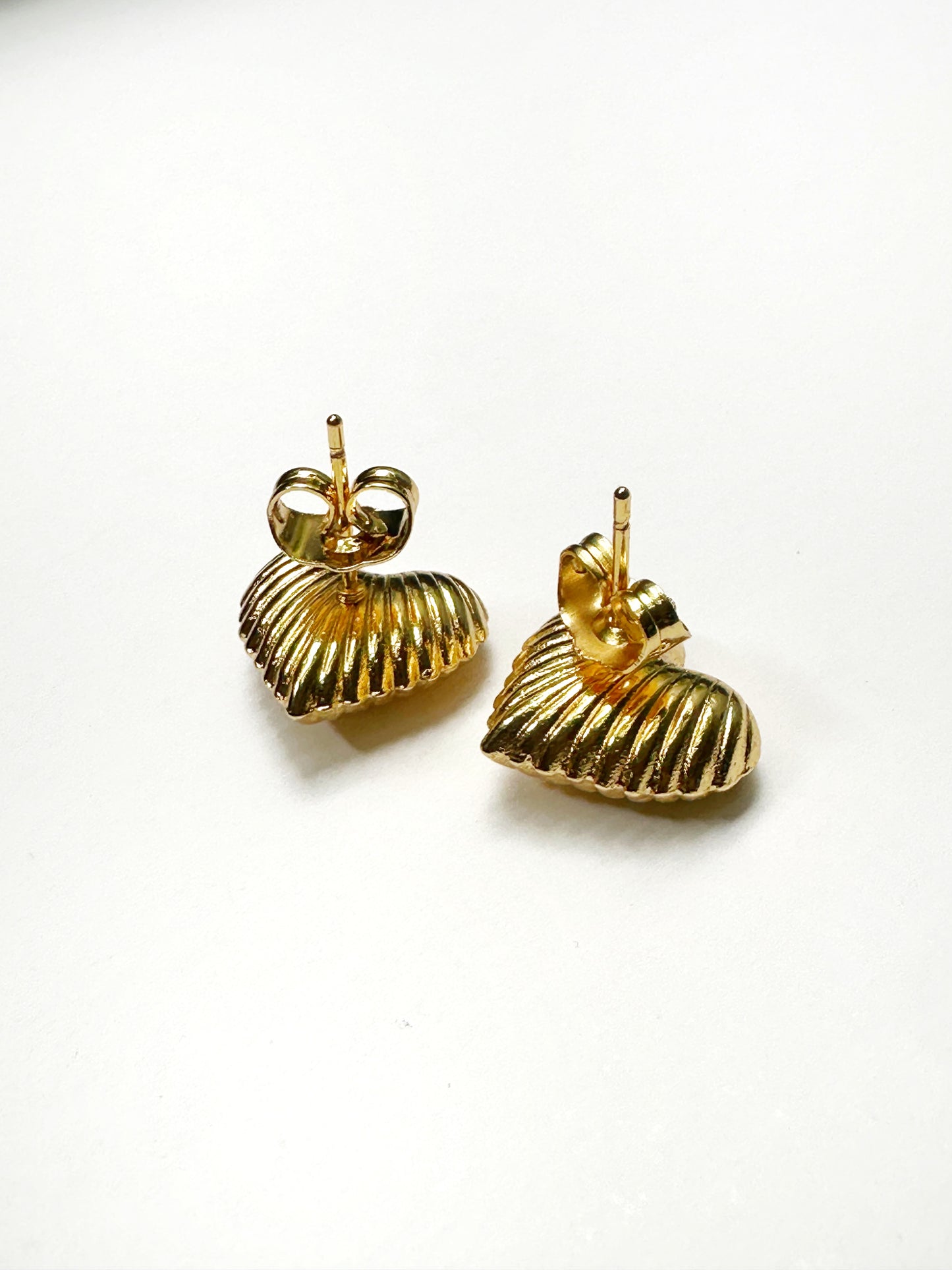 Flat lay showing back post of gold-tone ribbed heart earrings on white background