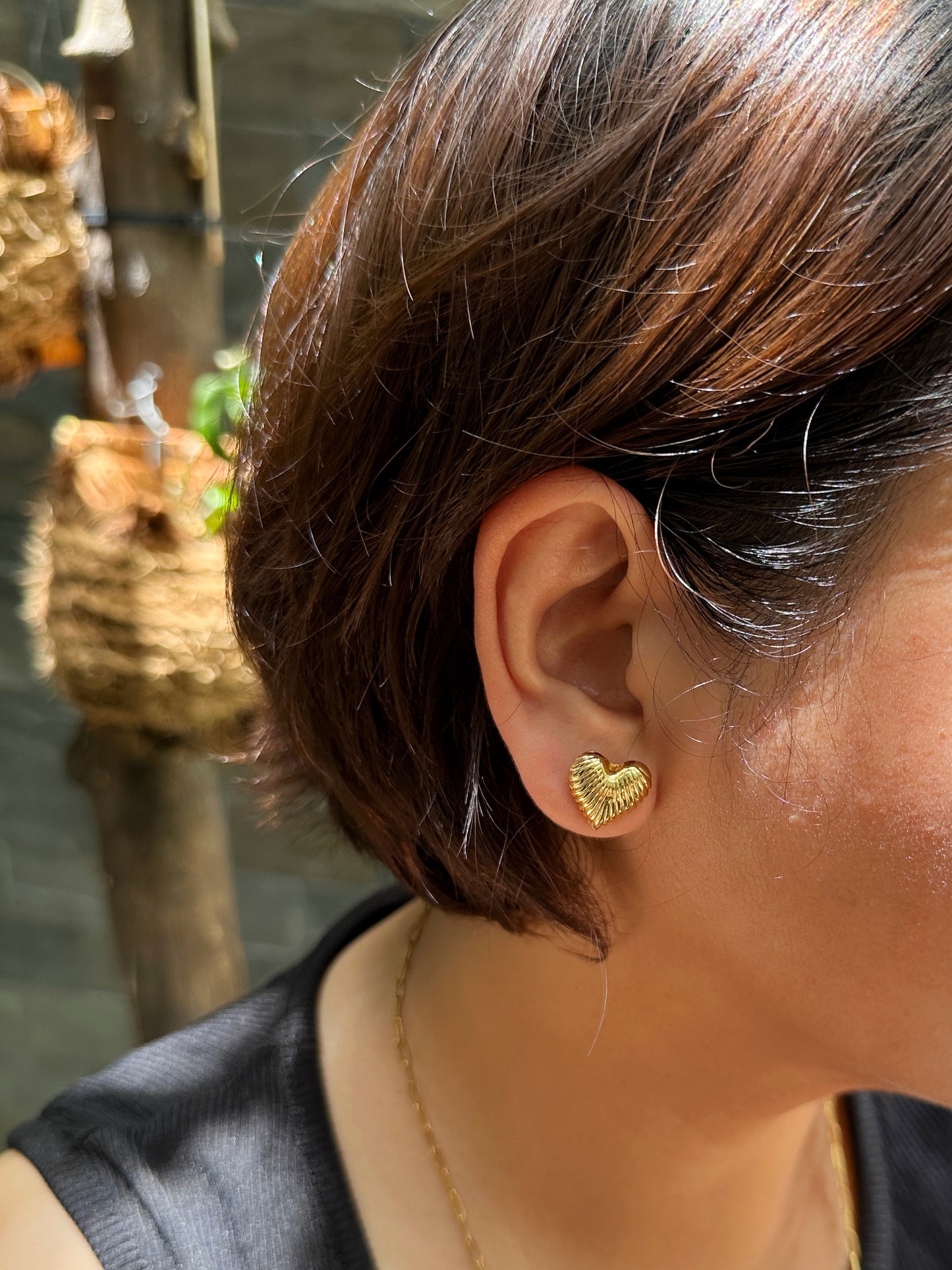 Side view of model wearing gold ribbed heart-shaped stud earrings