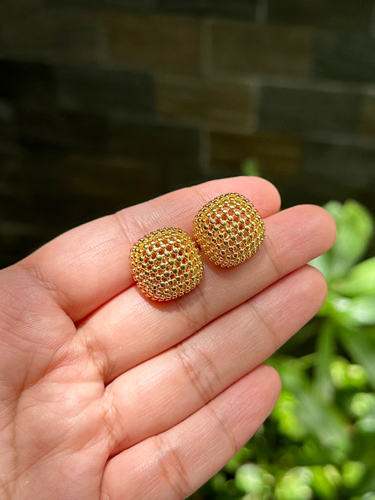 Gold-tone dome mesh earrings held in hand against green garden background