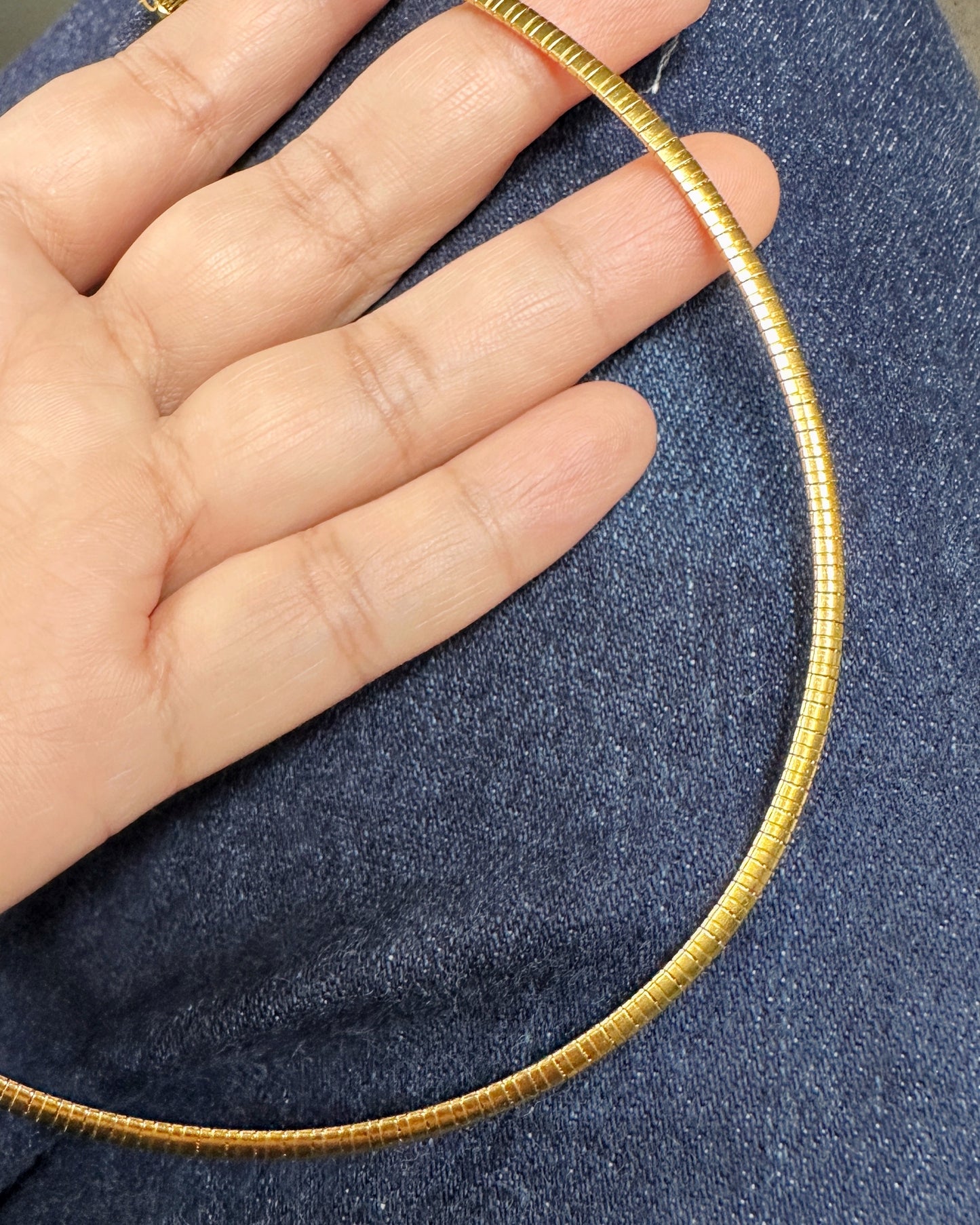 Gold snake chain necklace displayed against denim for scale