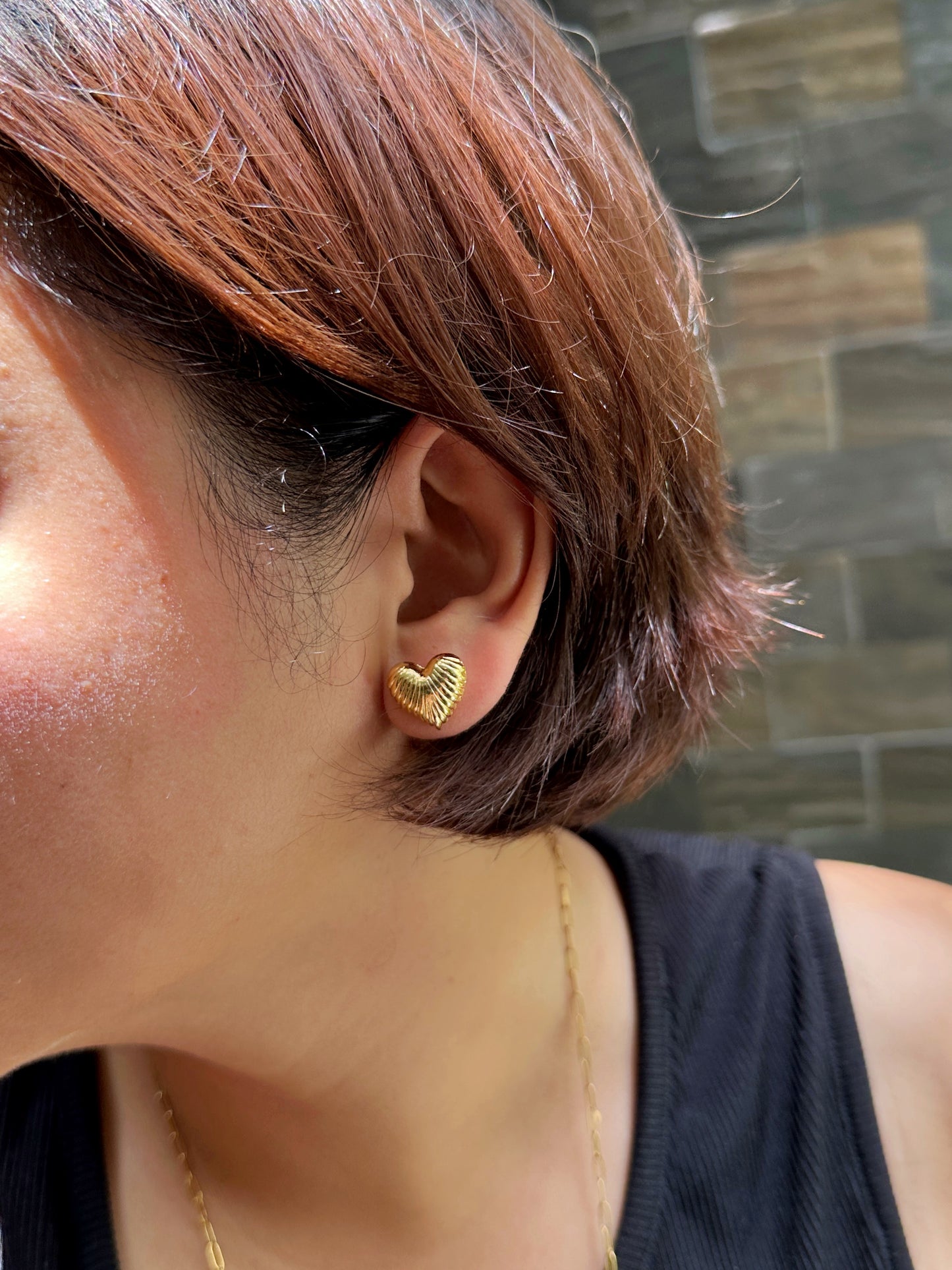 Close-up of gold-tone ribbed heart stud earring worn by a woman with short hair