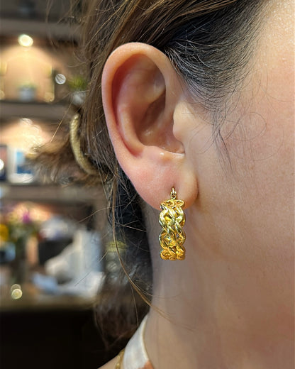 Close-up of a person wearing gold hoop earrings with a blurred indoor background.