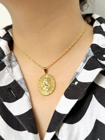 Close-up of a woman wearing a gold medallion pendant necklace on a rope chain, featuring a Greco-Roman profile design
