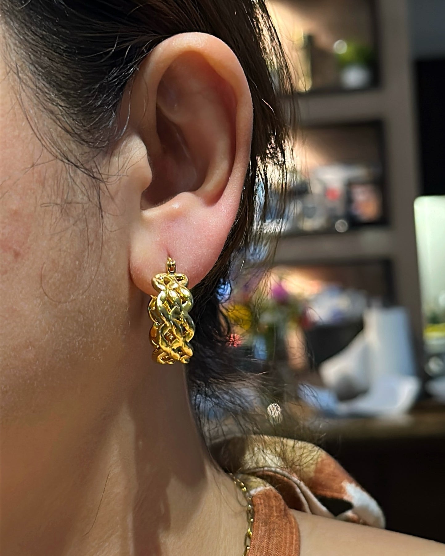 Close-up of an ear wearing a gold earring with a blurred indoor background