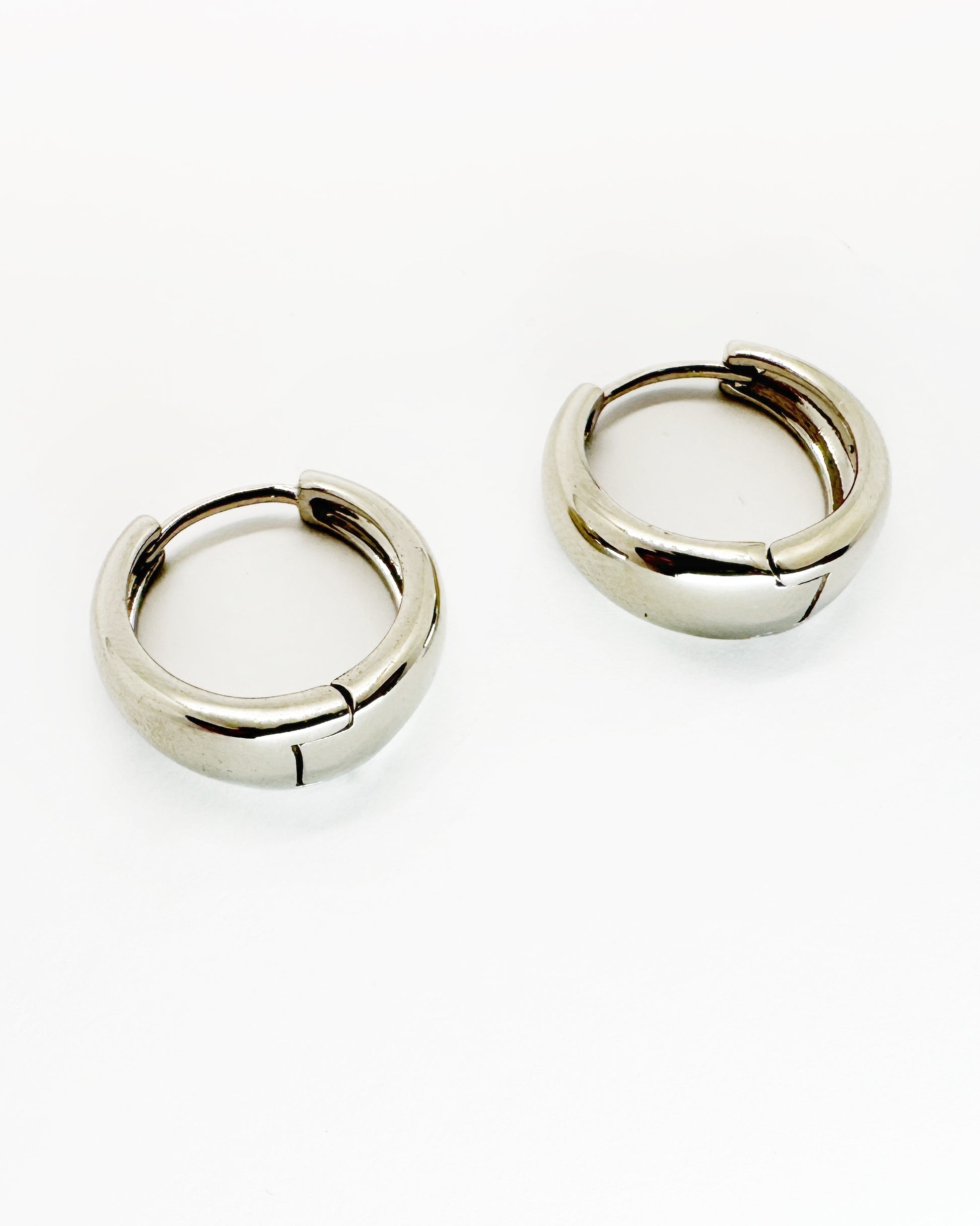 Angled view of cashew-shaped huggie earrings with polished white gold shine