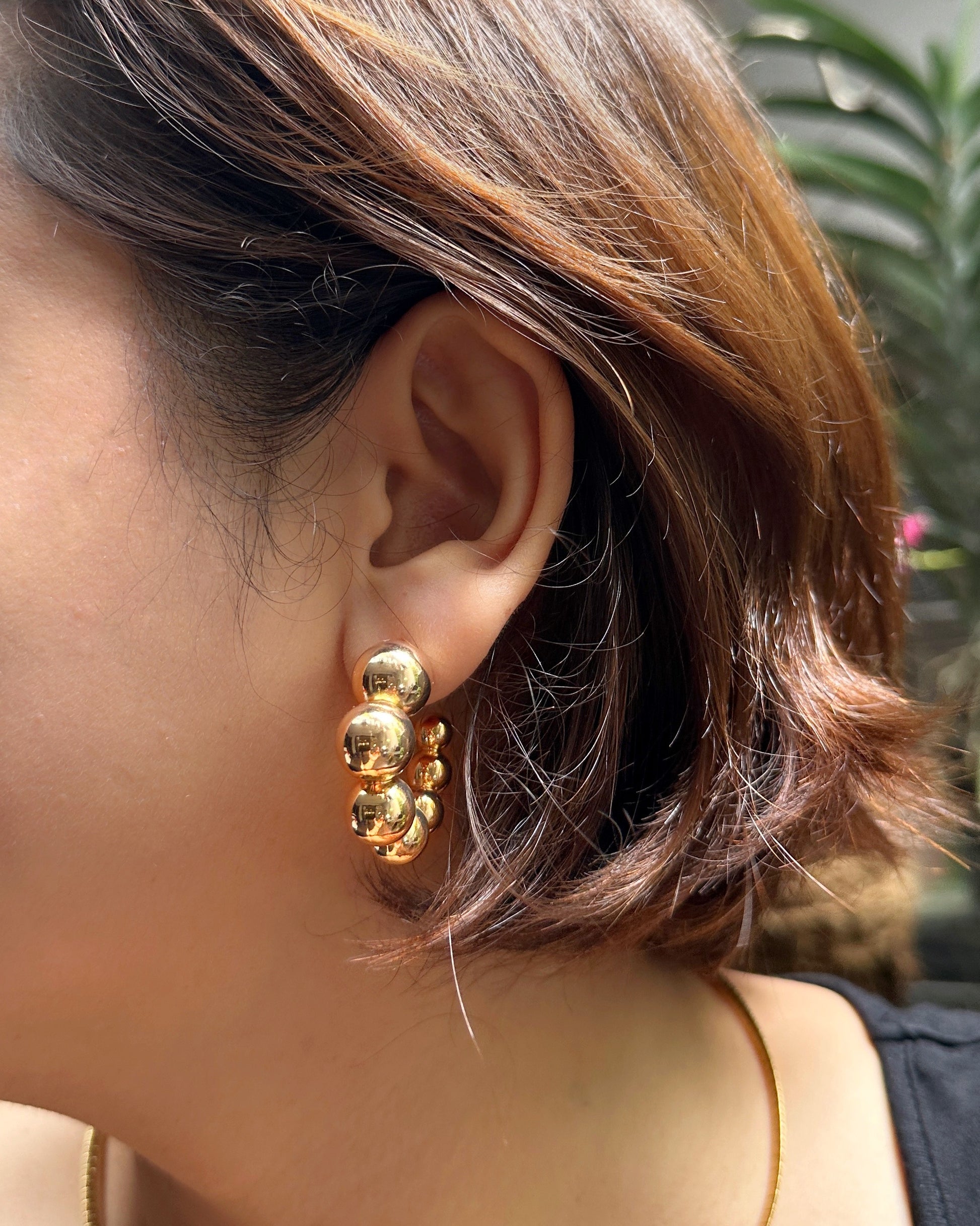 Woman wearing chunky gold statement hoop earrings with high-polish finish.