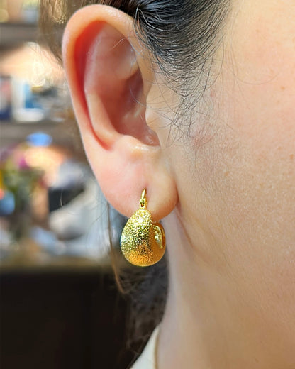 Gold teardrop earring worn by a person with a blurred background