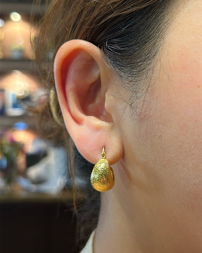 Close-up of a person wearing a gold teardrop earring with a blurred background.