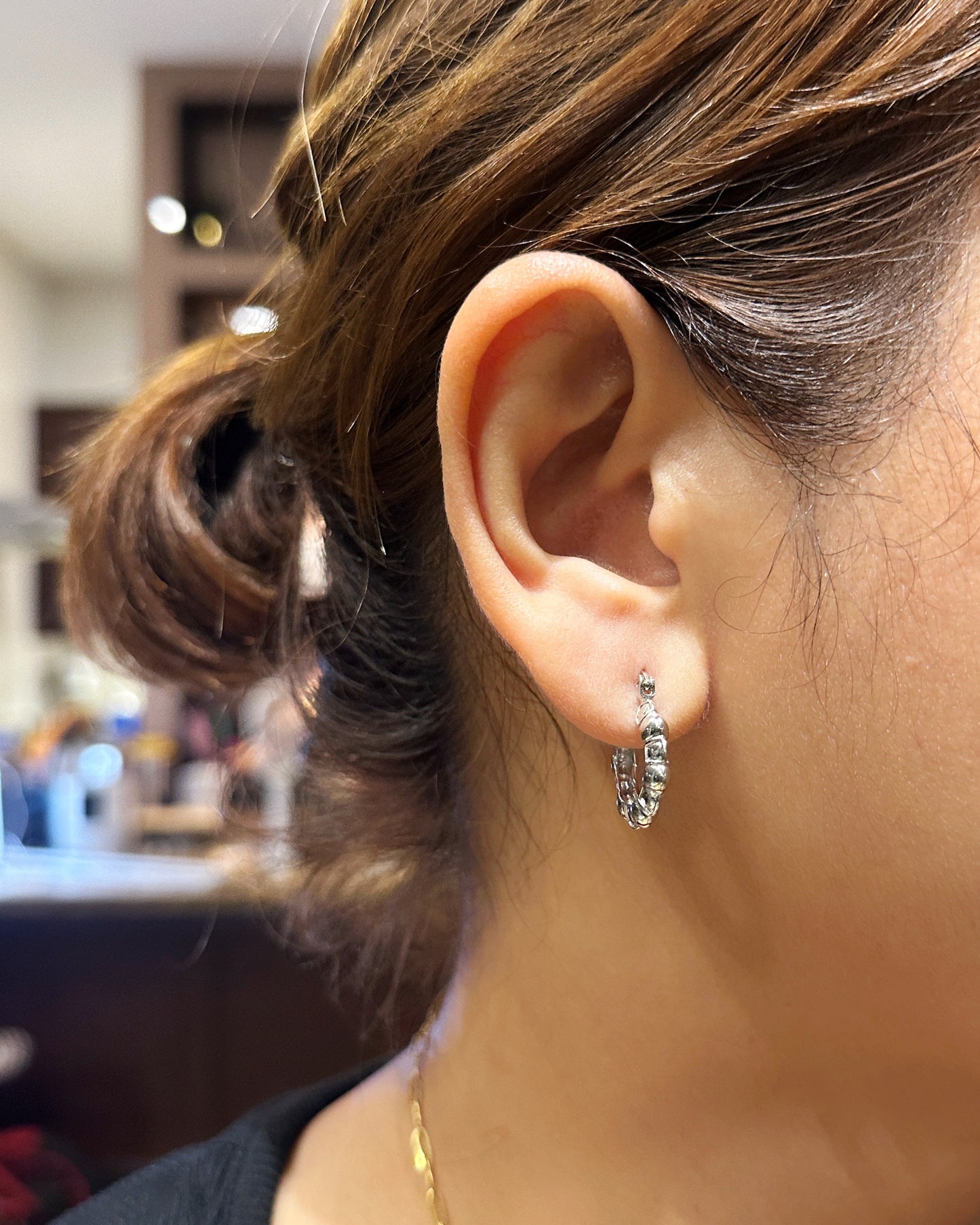 Model wearing sculpted pebble hoop earrings in white gold, showing true-to-size fit on ear