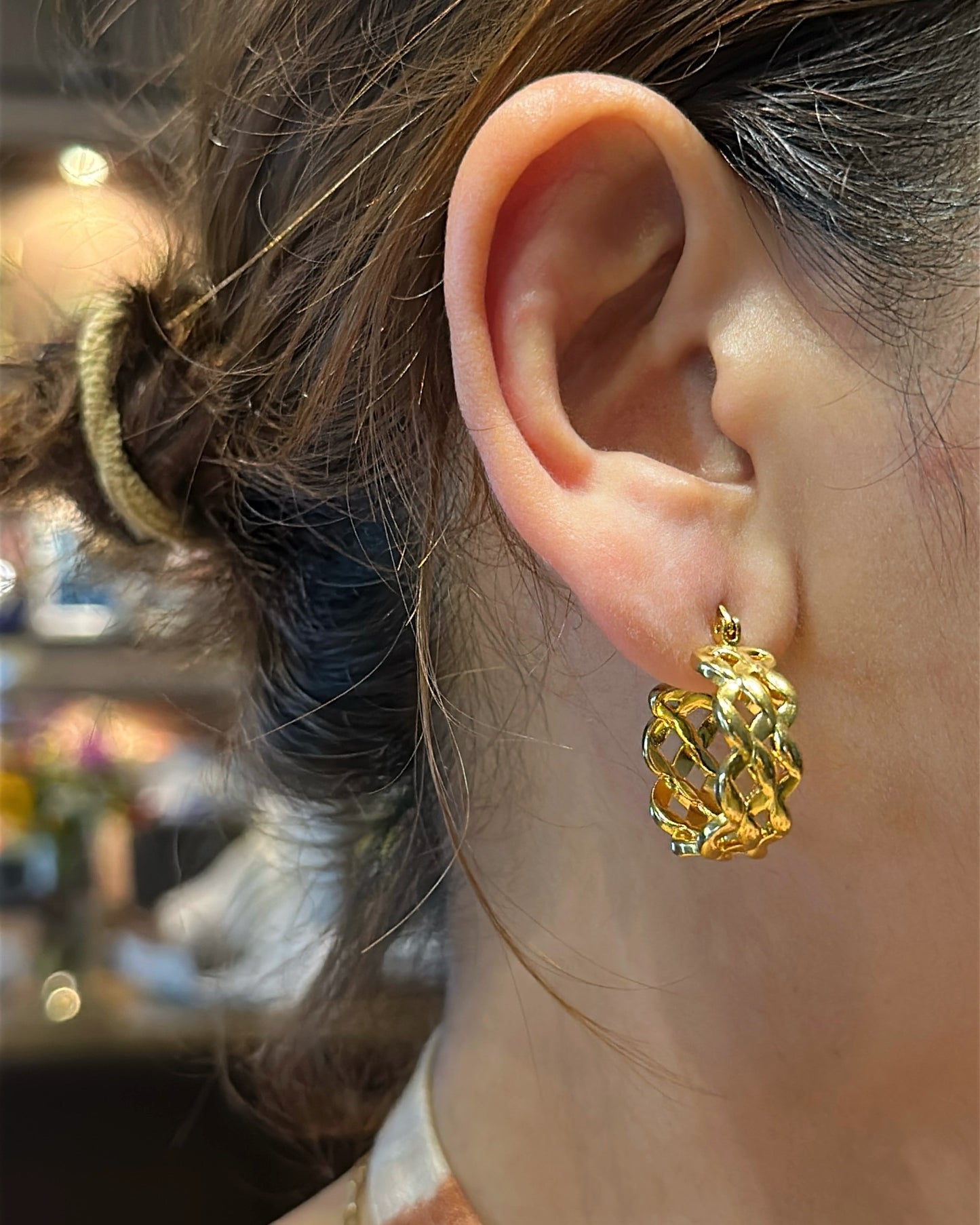 Close-up of a person wearing a gold earring with a blurred background
