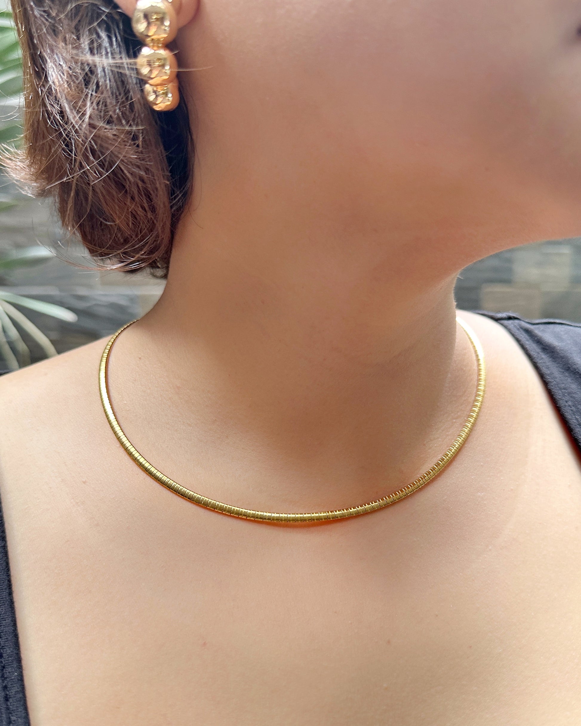 Model wearing flat snake chain necklace paired with chunky gold earrings